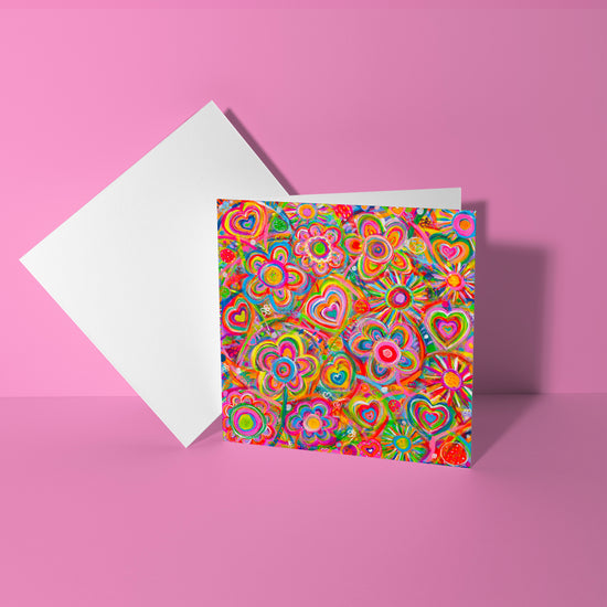 The Love in Neon Greeting Card by My Store features vibrant colors with multicolored floral and heart patterns on the cover, set against a pink background to evoke a sense of love.