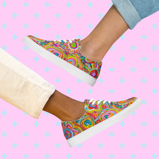 Two feet sport Love in Neon Canvas Sneakers by My Favourite Colour is Rainbow, with abstract patterns and white soles. The background features pink and light blue diamond shapes. Rolled-up jeans—one in light blue and the other in beige—add to the playful vibe.