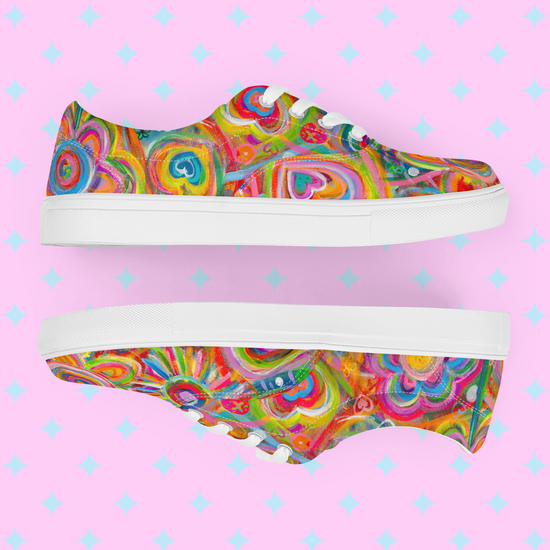 Displayed on a pastel pink background with white diamond shapes, the Love in Neon Canvas Sneakers by My Favourite Colour is Rainbow feature artistic patterns of hearts, swirls, and circles in vibrant pink, blue, green, and yellow. These eye-catching shoes boast white soles and laces.