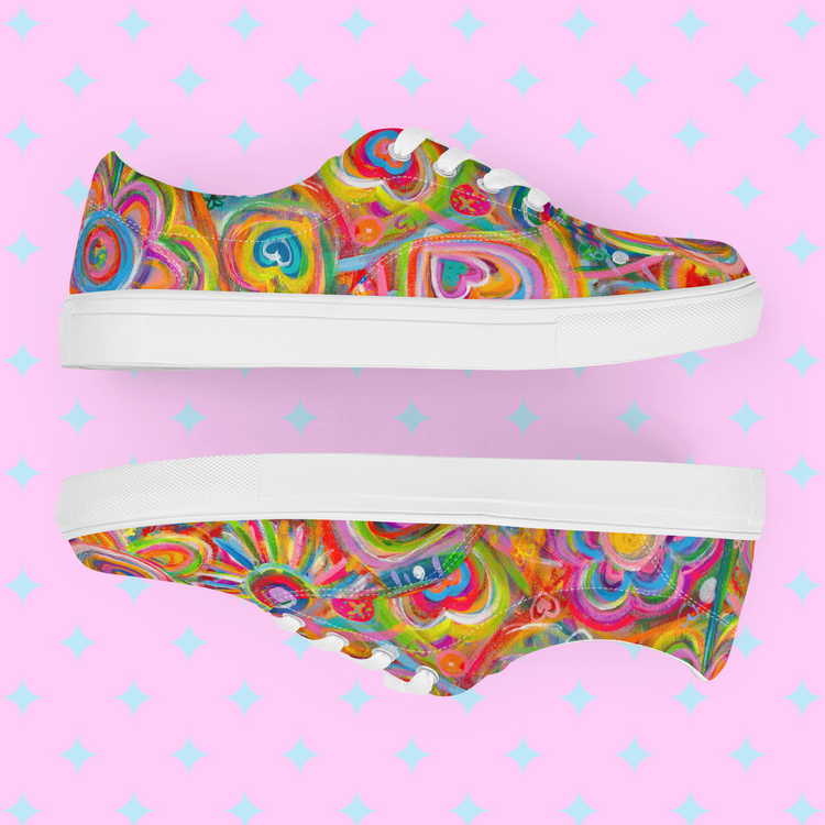 Displayed on a pastel pink background with white diamond shapes, the Love in Neon Canvas Sneakers by My Favourite Colour is Rainbow feature artistic patterns of hearts, swirls, and circles in vibrant pink, blue, green, and yellow. These eye-catching shoes boast white soles and laces.