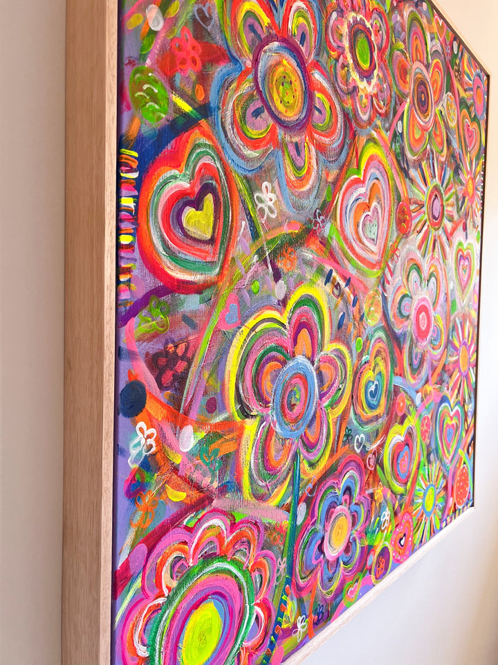 The Love In Neon Framed Original Painting by My Store is a colorful abstract with vibrant flowers and heart shapes in pink, green, blue, and neon tones. This acrylic artwork covers the entire surface and is elegantly set within a wooden frame.