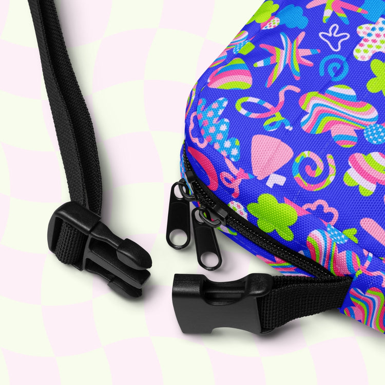 The Neon Carnival Mini Crossbody Bag by My Favourite Colour is Rainbow features vibrant blue with colorful abstract floral patterns, two zippers, and black adjustable straps with buckles against a light green and white checkered background.