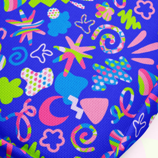 The Neon Carnival Mini Crossbody Bag by My Favourite Colour is Rainbow showcases a vibrant print with abstract shapes and symbols in pink, green, blue, and white on a royal blue background. Spirals, stars, and flower-like forms create a lively design perfect for any occasion.