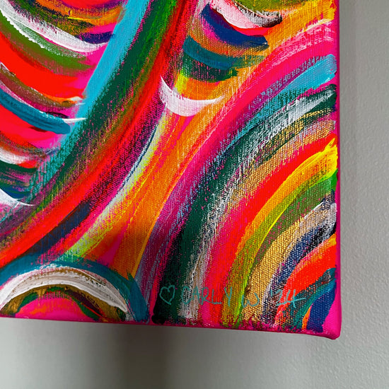 Close-up of the Neon Candy Floss Original Painting by My Store: vibrant acrylic on canvas with swirling neon pink, orange, green, and blue hues. A small outlined heart and signature adorn the bottom right corner. This dynamic rainbow artwork pops against a plain wall backdrop.