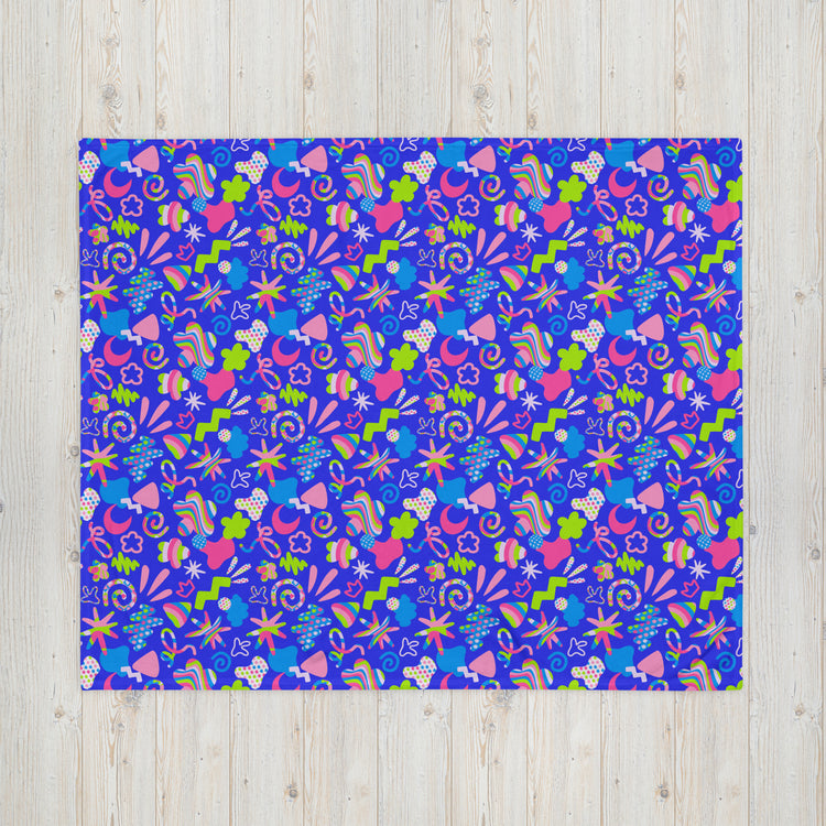 The Neon Carnival Throw Blanket by My Favourite Colour is Rainbow showcases a vibrant abstract pattern in pink, green, and purple with flowers, leaves, and swirls. Made from cosy fabric, its displayed flat on a light wood background.