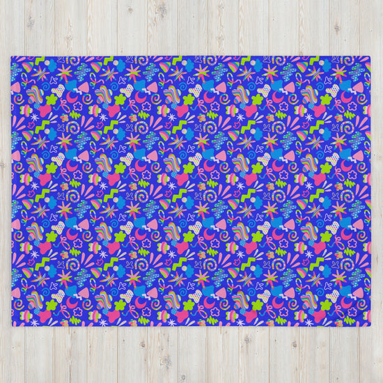 A vibrant rectangular rug on a light wooden floor features abstract shapes in bright blue, pink, green, and orange resembling flowers, leaves, and stars—a design akin to the My Favourite Colour is Rainbow Neon Carnival Throw Blanket.