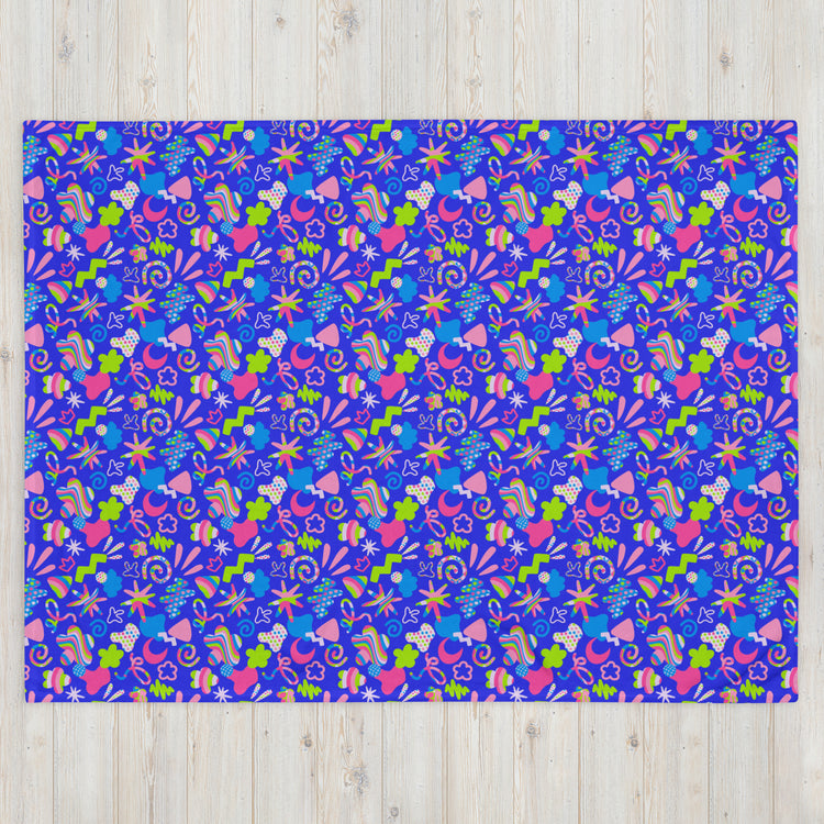 A vibrant rectangular rug on a light wooden floor features abstract shapes in bright blue, pink, green, and orange resembling flowers, leaves, and stars—a design akin to the My Favourite Colour is Rainbow Neon Carnival Throw Blanket.