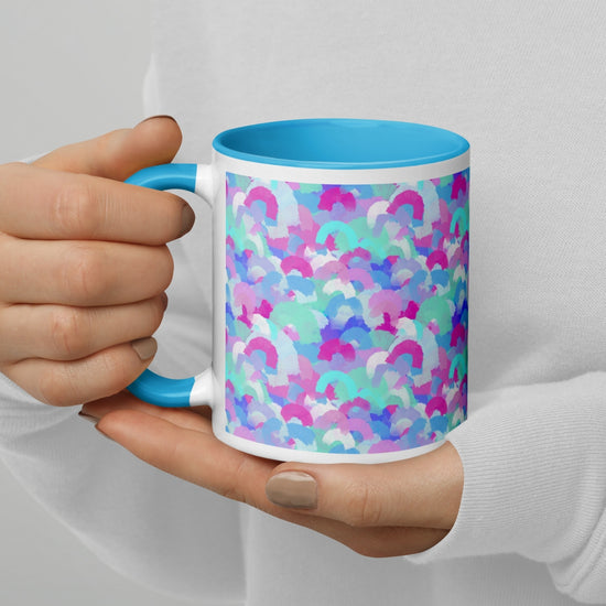 A person with beige nails and a white sweatshirt holds the Pastel Rainbow Mug by My Favourite Colour is Rainbow, featuring a light blue handle and rim adorned with soft watercolour rainbows in pink, blue, aqua and white.
