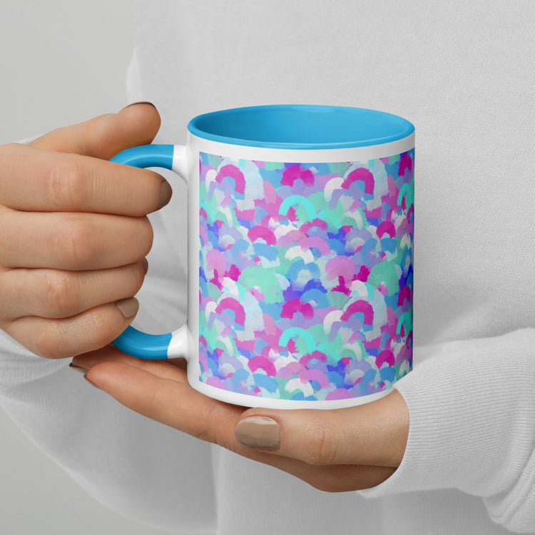 A person with beige nails and a white sweatshirt holds the Pastel Rainbow Mug by My Favourite Colour is Rainbow, featuring a light blue handle and rim adorned with soft watercolour rainbows in pink, blue, aqua and white.