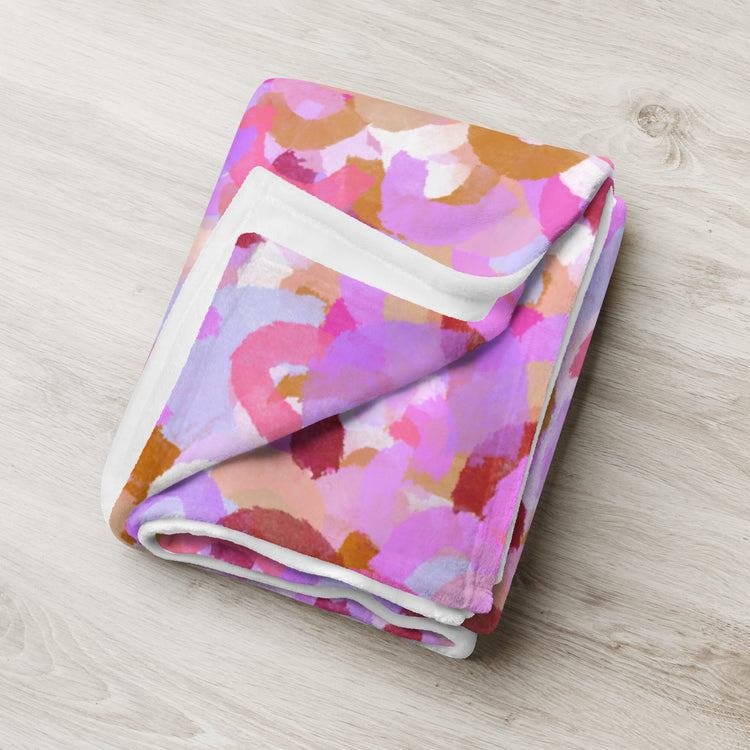 The Pink Rainbow Throw Blanket by My Favourite Colour is Rainbow features a vibrant abstract pattern with overlapping watercolor-style circles in shades of pink, purple, orange, and beige on a light wood surface, making it a stylish décor piece for any room.