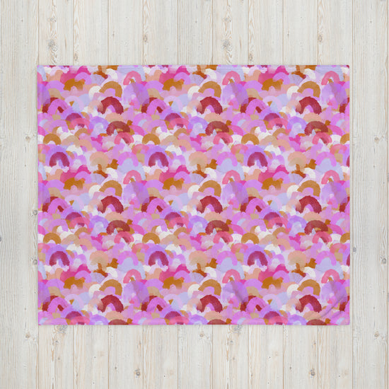 The Pink Rainbow Throw Blanket by My Favourite Colour is Rainbow showcases a vibrant pattern of abstract semicircles in pink, orange, red, and white. Its cozy texture enhances any light wooden surface with visible grain, making it perfect for stylish décor.