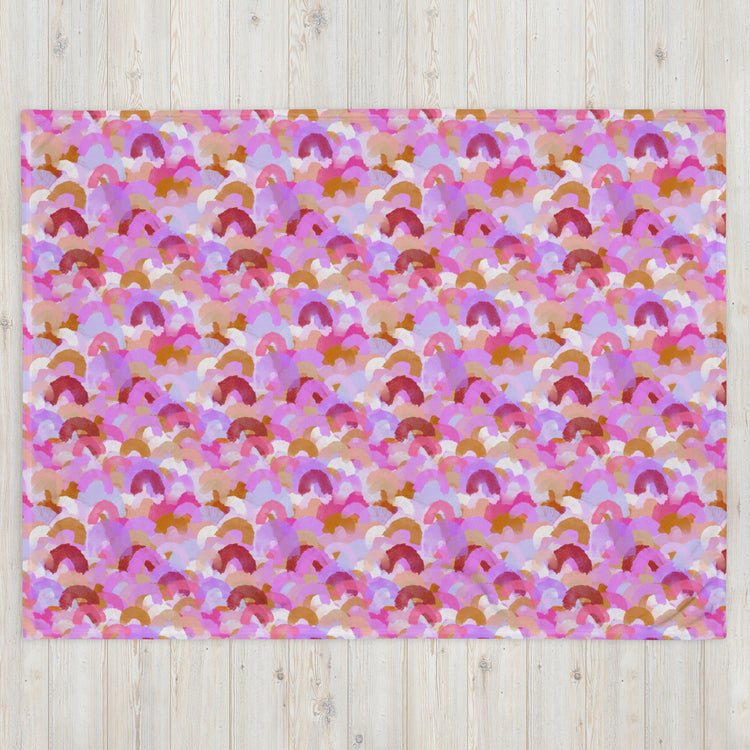 The Pink Rainbow Throw Blanket by My Favourite Colour is Rainbow, with its vibrant pattern of overlapping arches in pink, purple, brown, and white tones, beautifully complements the stylish décor on a light wooden floor.