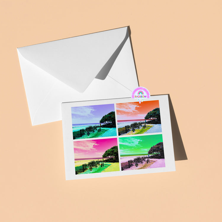 The My Store Pohutukawa Pop Art greeting card (Version 2) showcases a vibrant New Zealand beach scene in four panels tinted blue, purple, pink, and green. Paired with a white envelope, its elegantly set on a light tan background.