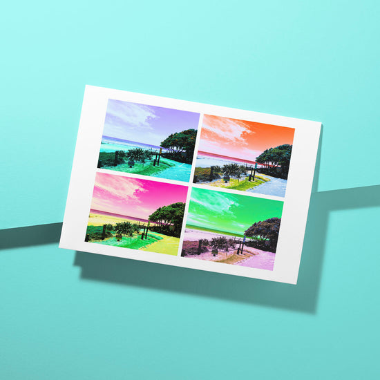 The Pohutukawa Pop Art greeting card (Version 2) from My Store showcases four sections of the same New Zealand beach scene—with boardwalk, trees, and ocean—using vibrant purple, orange, green, and pink filters. This eye-catching design stands out against a blue background.