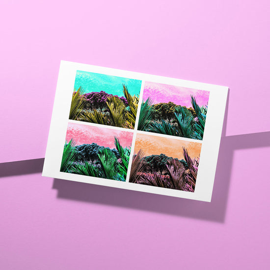 A vibrant greeting card, the Pohutukawa Pop Art (Version 3) from My Store, features four tropical-themed images with brilliant palm leaves and colorful skies on a textured pink surface, capturing New Zealands spirit.