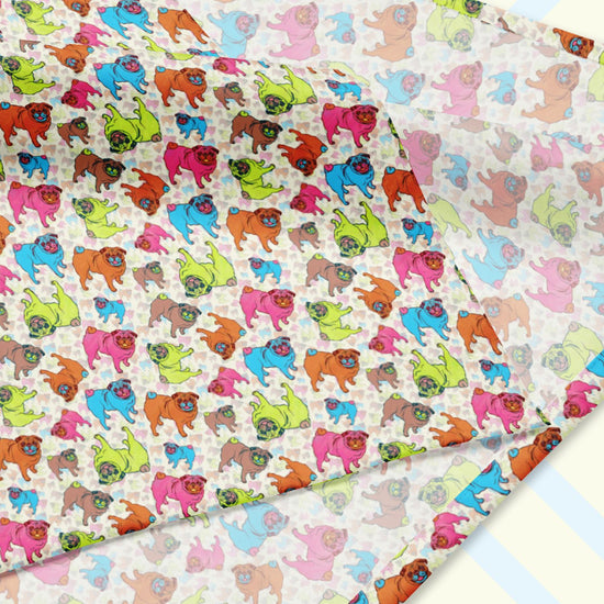 A closeup of the 'Pugalicious' Bandana by My Favourite Colour is Rainbow featuring a design of vibrant orange, blue, green, and pink pugs on a pale yellow background. The design is printed on only one side of the bandana.