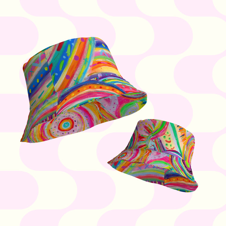 Two reversible bucket hats, The Rainbow Connection/Summer Sorbet by My Favourite Colour is Rainbow, feature abstract swirls and dots in vibrant rainbow hues on a pastel pink and white background, perfect for adding a playful and artistic touch to your style.
