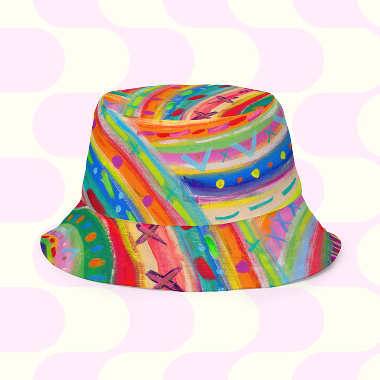 The Rainbow Connection/Summer Sorbet Reversible Bucket Hat by My Favourite Colour is Rainbow features vibrant abstract patterns in red, blue, yellow, green, and purple with a soft pink circular design background. Available in multiple sizes for your style BFF.