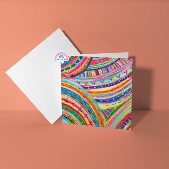The Rainbow Connection Greeting Card by My Store showcases vibrant abstract rainbow patterns and geometric designs on high-quality card stock, set against a plain peach background with an open white envelope beside it.