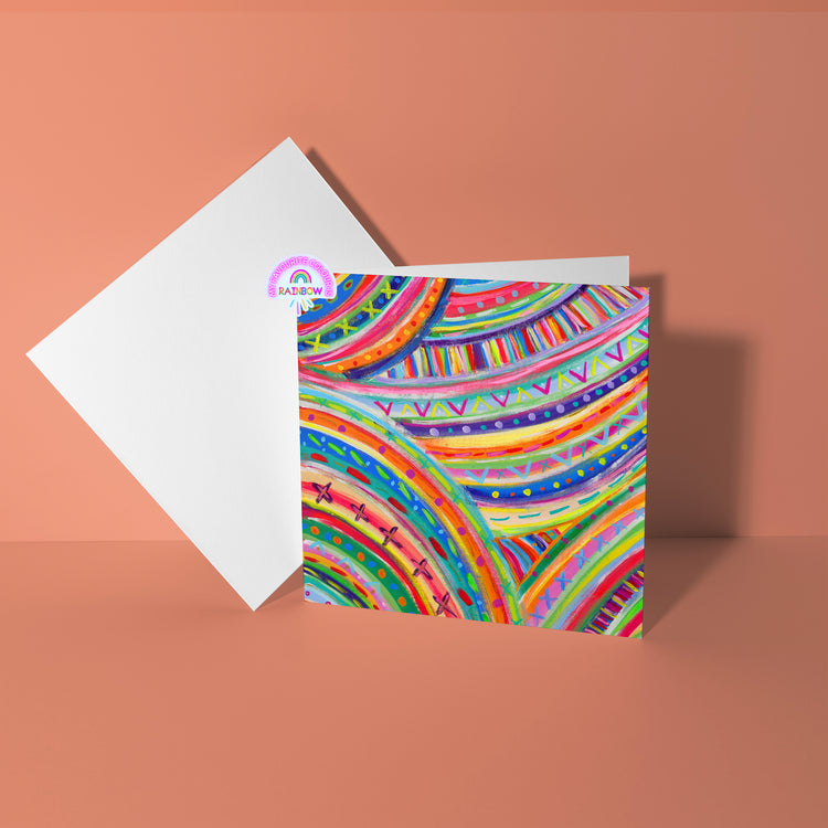 The Rainbow Connection Greeting Card by My Store showcases vibrant abstract rainbow patterns and geometric designs on high-quality card stock, set against a plain peach background with an open white envelope beside it.