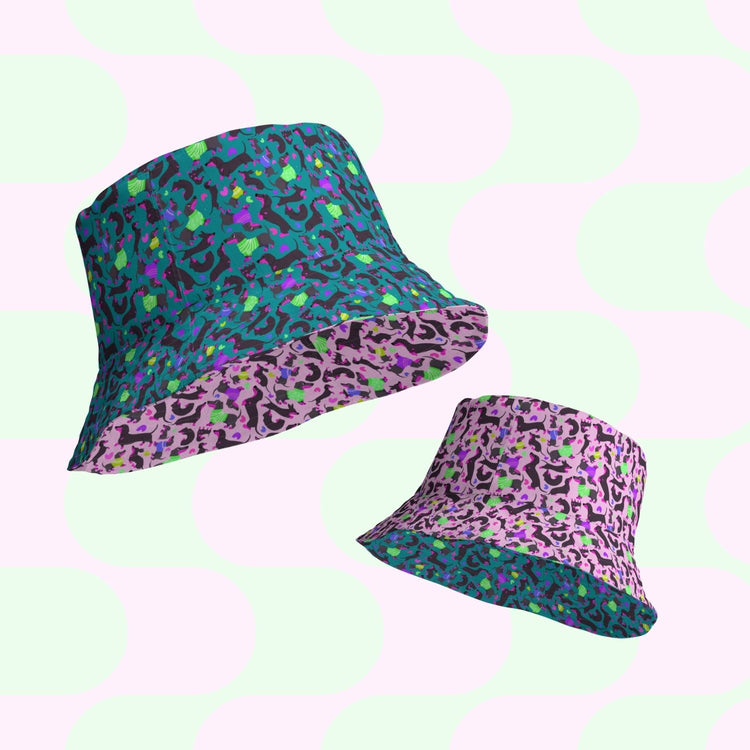 Two reversible bucket hats from My Favourite Colour is Rainbow combine style and comfort, featuring abstract patterns. One hat is blue and green, the other purple and pink. Floating on a pastel background with large rounded polka dot shapes, they exude a modern, vibrant look as playful as Silly Sausages.