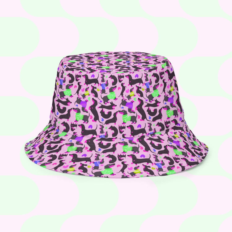 Explore the Silly Sausages Green/Pink Reversible Bucket Hat by My Favourite Colour is Rainbow. This stylish, comfortable hat features colorful abstract patterns with pink, green, black, and purple shapes and a pastel green and pink overlapping circle background for playful flair.