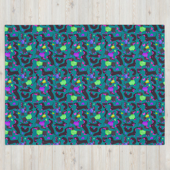 The Silly Sausages Throw Blanket - Green from My Favourite Colour is Rainbow features a vibrant pattern of abstract dinosaurs in green, blue, purple, and black on teal. Perfect for warmth, it combines playful dinosaur shapes with geometric elements for a dynamic touch to your space.