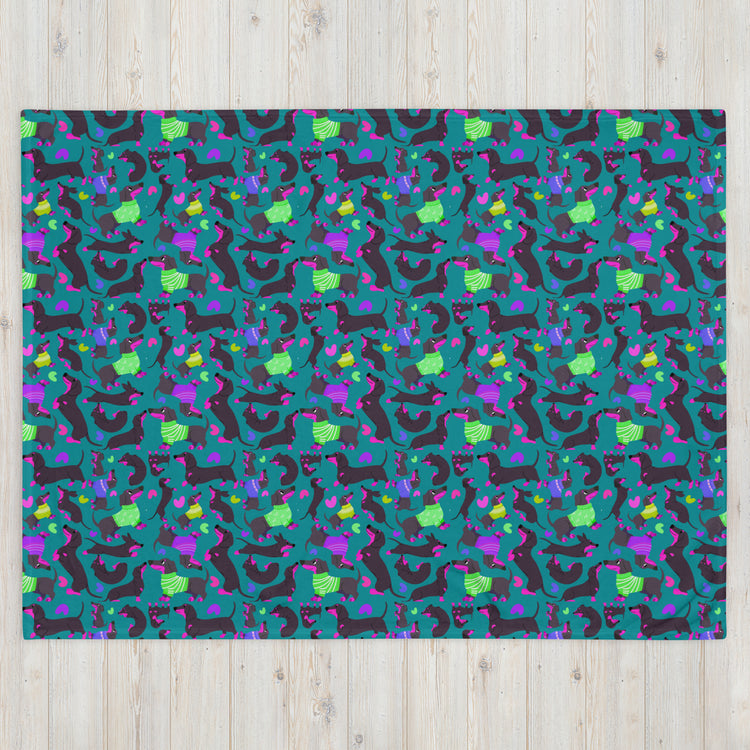 The Silly Sausages Throw Blanket - Green from My Favourite Colour is Rainbow features a vibrant pattern of abstract dinosaurs in green, blue, purple, and black on teal. Perfect for warmth, it combines playful dinosaur shapes with geometric elements for a dynamic touch to your space.