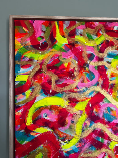 The Spaghetti Junction Framed Original Painting by My Store features vibrant swirling patterns in red, yellow, pink, green, and blue. Enhanced with neon and gold tones and a textured finish, this artwork is elegantly framed in wood against a gray wall.