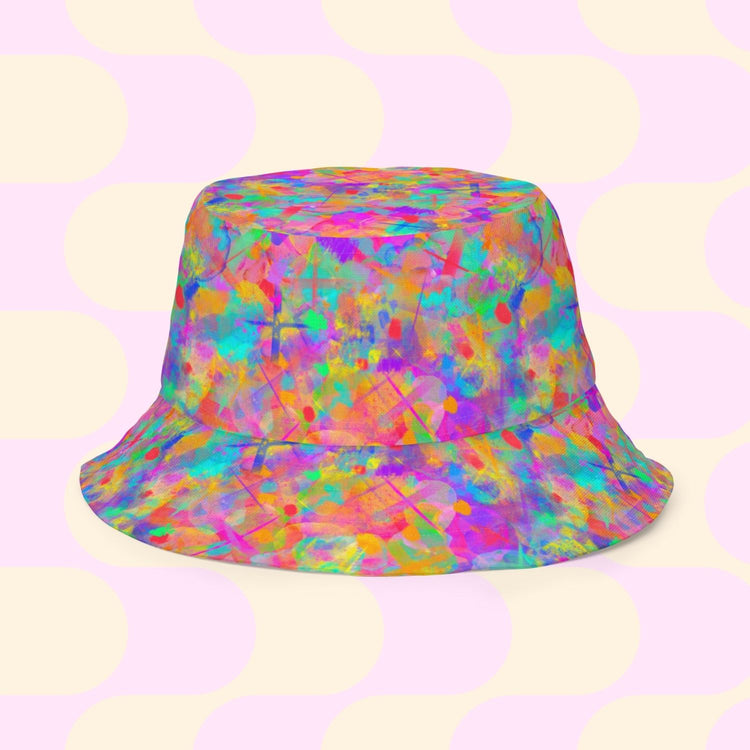 The Splotches and Crosses Reversible Bucket Hat by My Favourite Colour is Rainbow features a vibrant watercolor pattern in pink, orange, blue, and green with light yellow circles on a pale pink background. Available in multiple sizes, its the perfect style BFF for any outfit.
