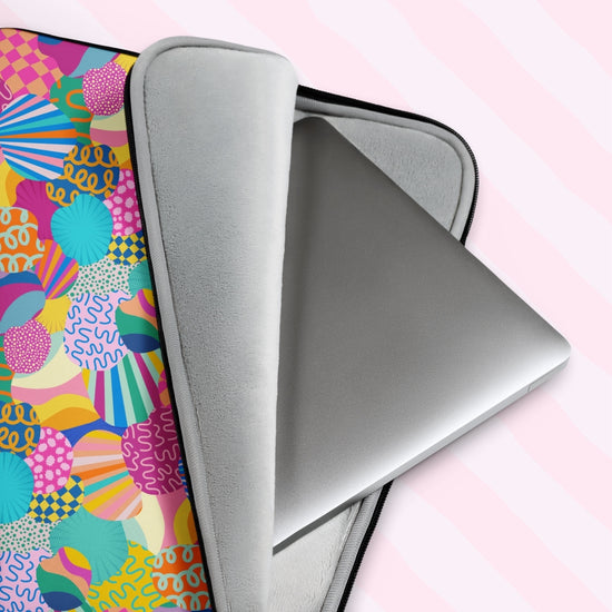 A laptop peeks out of the My Favourite Colour is Rainbows Squiggs and Stripes Laptop Sleeve, featuring an abstract design of colourful geometric shapes, stripes and squiggles in pink, blue, orange yellow, and green, creating a bold tech statement.  It has a great padded interior to keep your laptop safe from scratches. 
 The print is on only one side of the laptop sleeve, the other side is black.  The laptop sleeve is shown on a pastel background.