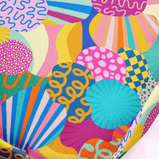 The Squiggs and Stripes Mini Crossbody Bag by My Favourite Colour is Rainbow features a vibrant, abstract pattern of overlapping shapes like circles, stripes, and swirls in pink, blue, yellow, orange, and green. Its adjustable straps ensure comfort while creating a playful visual effect.