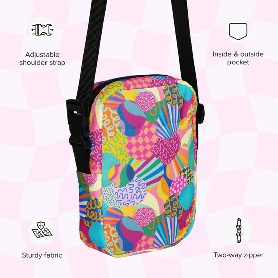The Squiggs and Stripes Mini Crossbody bag by My Favourite Colour is Rainbow is a sturdy, water-resistant crossbody bag with a vibrant abstract design. It features an adjustable shoulder strap, two-way zipper, and both interior and exterior pockets, highlighted by surrounding feature icons.