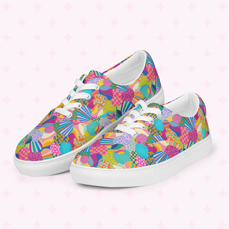 The Squiggs and Stripes Canvas Sneakers by My Favourite Colour is Rainbow feature a vibrant abstract pattern with pink, blue, yellow, and green shapes and lines on a light pink background with subtle star designs. They have white laces and soles for added style.