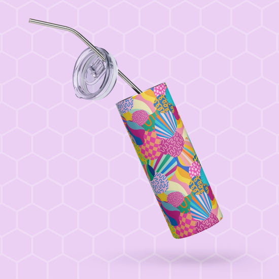 The Squiggs and Stripes Stainless Steel Tumbler by My Favourite Colour is Rainbow, featuring a metal straw and colorful abstract design, stands upright on a hexagonal lavender background, with its transparent lid partially open.