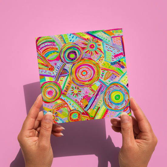 Two hands display the Summer Sorbet Greeting Card by My Favourite Colour is Rainbow, featuring a vibrant abstract design with circular patterns in green, yellow, orange, blue, and pink on high-quality cardstock.