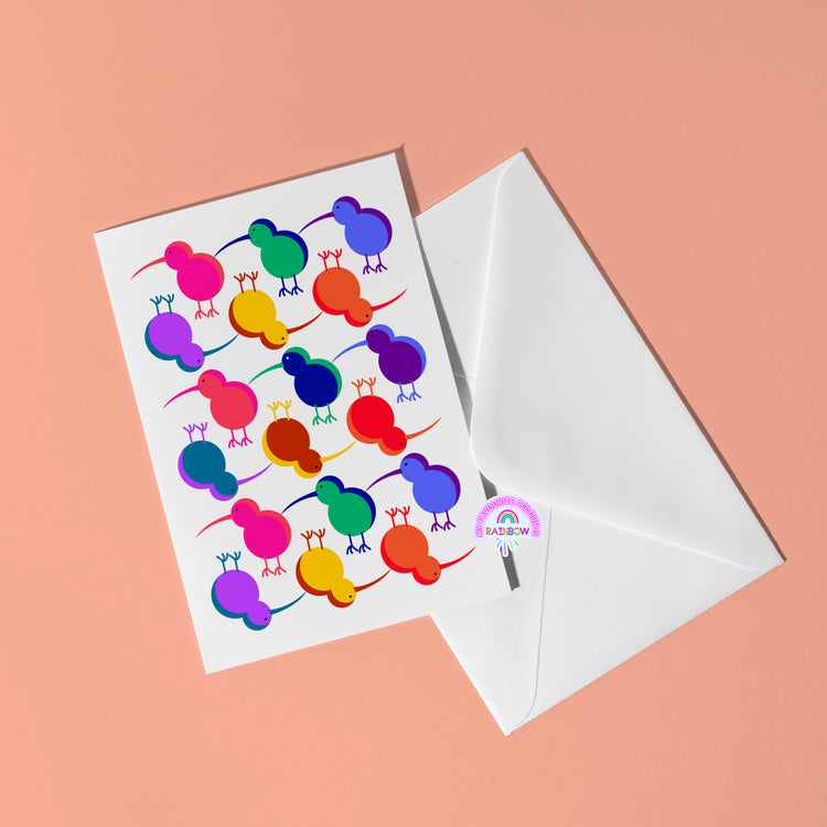 The Technicolour Kiwi greeting card from My Store rests on a peach surface, displaying vibrant, stylized birds in rows. Next to it is an open white envelope featuring a logo with a small rainbow and the word RAINBOW—ideal for brightening someones day.