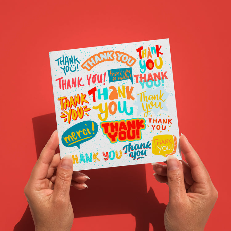 Hands hold a cheerful My Store Thank You Typography Card featuring vibrant Thank You messages in various colors and fonts on a red background.