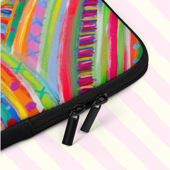 A closeup of The Rainbow Connection Laptop Sleeve by My Favourite Colour is Rainbow.  The sleeve features a colourful abstract design of curved lines, dots, and triangles in vibrant pink, orange, green, blue, and yellow.  It includes a black padded binding with dual zipper pull tabs for added convenience.  The print is on only one side of the laptop sleeve, the other side is black.   It is shown on a pastel background.