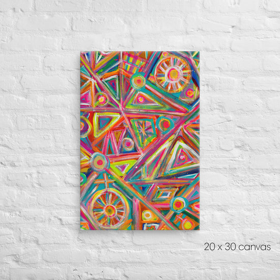 The Tropical Geometry Canvas Artwork by My Favourite Colour is Rainbow decorates a white brick wall with vibrant geometric patterns, featuring triangles, circles, and lines in pink, orange, green, and blue hues. The reproduction measures 20 x 30 inches.