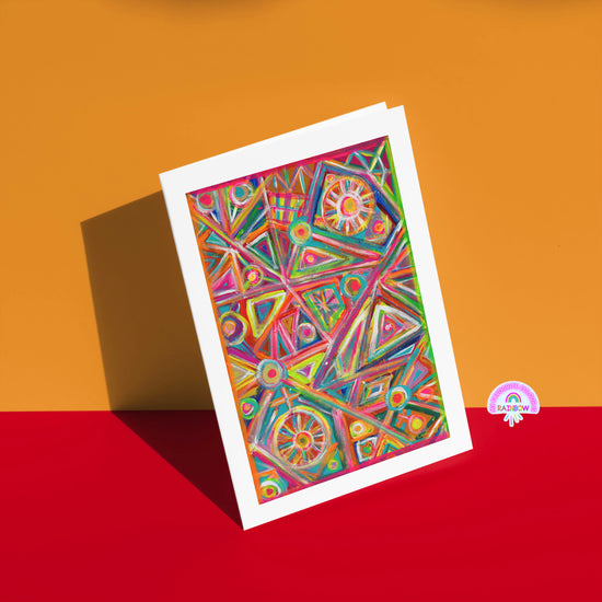 The Tropical Geometry Greeting Card by My Store displays bold triangles, circles, and lines on a vivid orange and red background with a small RAINBOW logo in the bottom right corner.