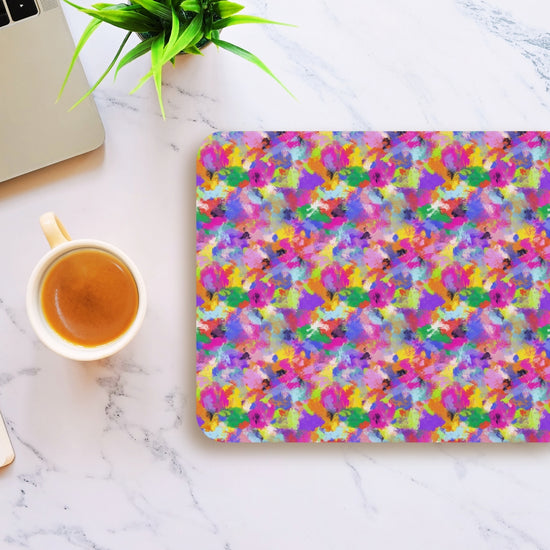 The Watercolour Rainbow Mouse Pad by My Favourite Colour is Rainbow adds a vibrant touch to a white marble desk, featuring splashes of purple, pink, yellow, and blue beside a laptop, coffee cup, and small green plant.