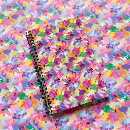 The My Stores spiral-bound Watercolour Rainbow Notebook boasts a vibrant, abstract cover with bright pink, yellow, green, and blue hues. It blends seamlessly on a matching background and is part of our stationery collection, perfect for sparking creativity.