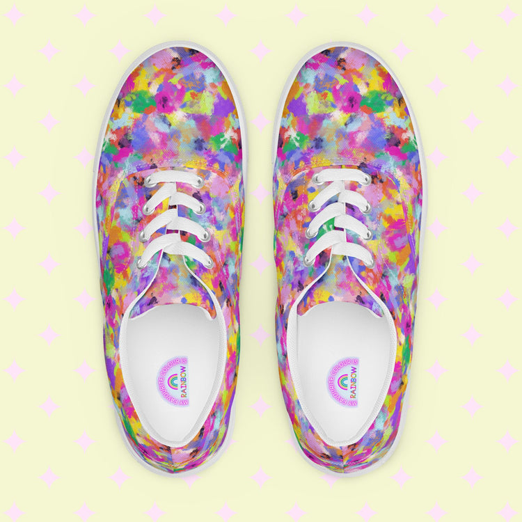 The Watercolour Rainbow Canvas Sneakers by My Favourite Colour is Rainbow showcase a vibrant abstract pattern in pink, blue, yellow, and green hues. White laces and soles contrast against a pale backdrop with subtle pink diamonds, offering a top-down view that highlights their colorful style.