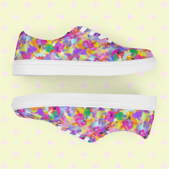 The Watercolour Rainbow Canvas Sneakers from My Favourite Colour is Rainbow showcase an abstract design in pink, purple, yellow, blue, and green. Displayed side by side on a yellow backdrop with pink diamond shapes, these vibrant sneakers have white laces and soles.