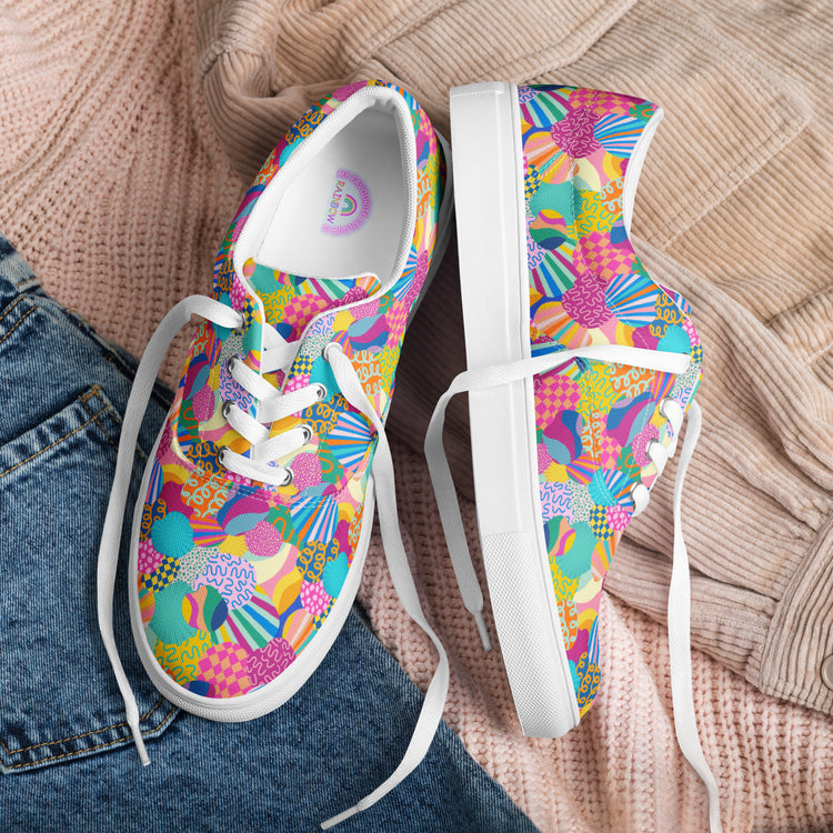 Squiggs and Stripes Canvas Sneakers by My Favourite Colour is Rainbow, featuring a comfy fit with abstract patterns in pink, green, yellow, and blue on white rubber soles and laces, are showcased on a beige knitted sweater paired with blue denim jeans.