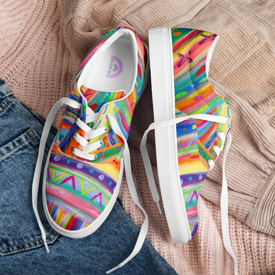 The Rainbow Connection Canvas Sneakers by My Favourite Colour is Rainbow, featuring abstract patterns and white laces, stylishly accompany a cozy light brown knit sweater and blue denim jeans, showcasing a vibrant style.