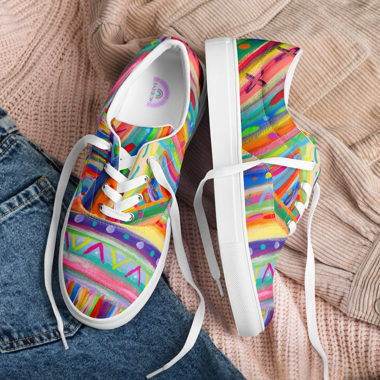 The Rainbow Connection Canvas Sneakers by My Favourite Colour is Rainbow, featuring abstract patterns and white laces, stylishly accompany a cozy light brown knit sweater and blue denim jeans, showcasing a vibrant style.