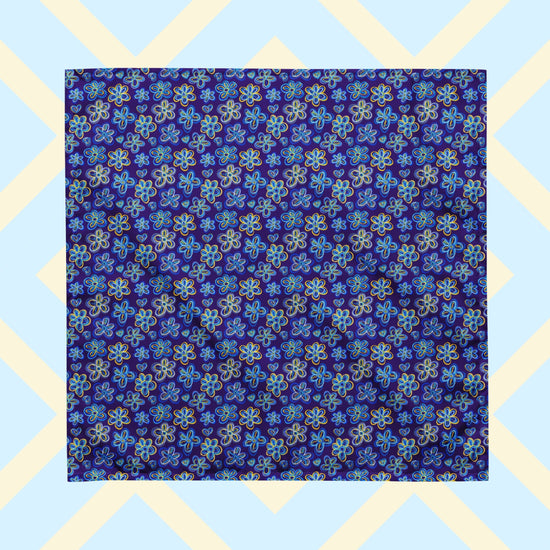 The Bloomscape Bandana by My Favourite Colour is Rainbow features a design of large flowers and small hearts in shades of blue and yellow on a royal blue background. 