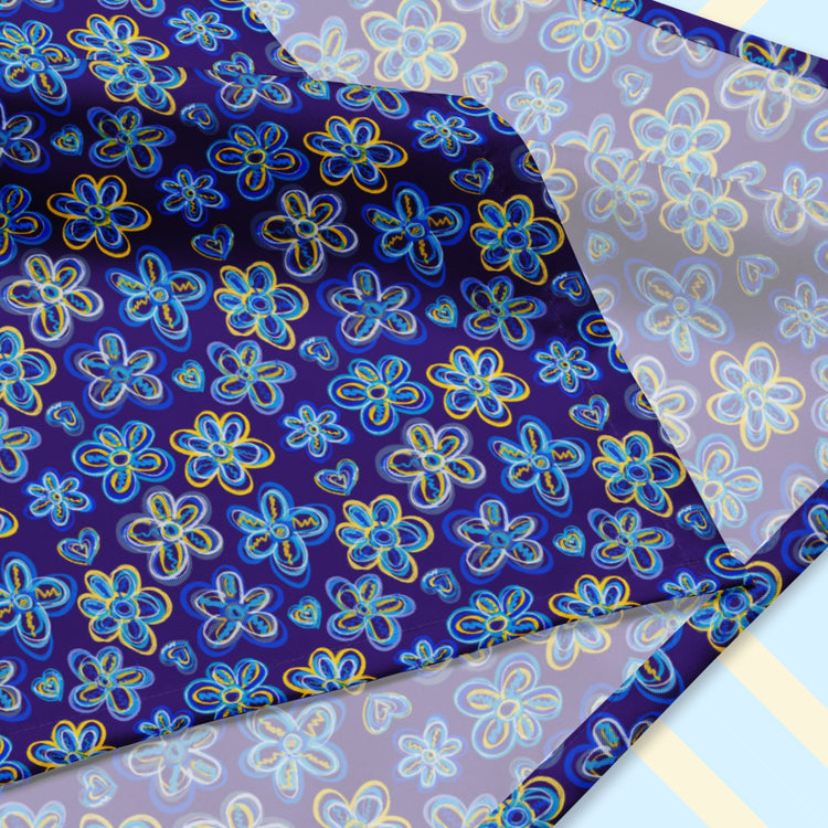 The Bloomscape Bandana by My Favourite Colour is Rainbow features a design of large flowers and small hearts in shades of blue and yellow on a royal blue background.  The design is on only one side of the bandana.